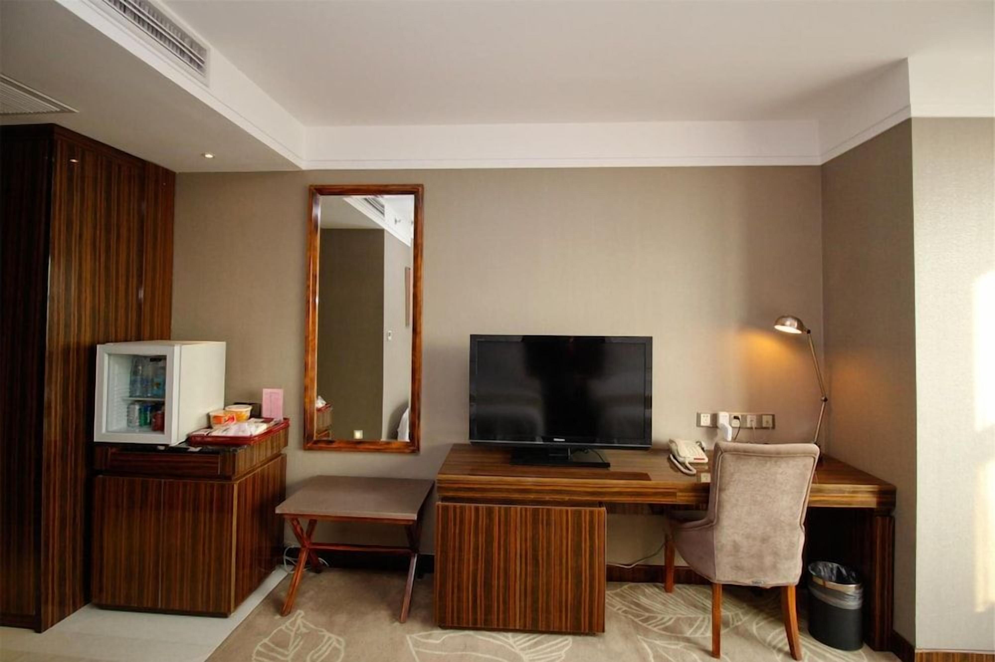 Habitación de hotel con un escritorio de madera, televisor, espejo y basurero.
