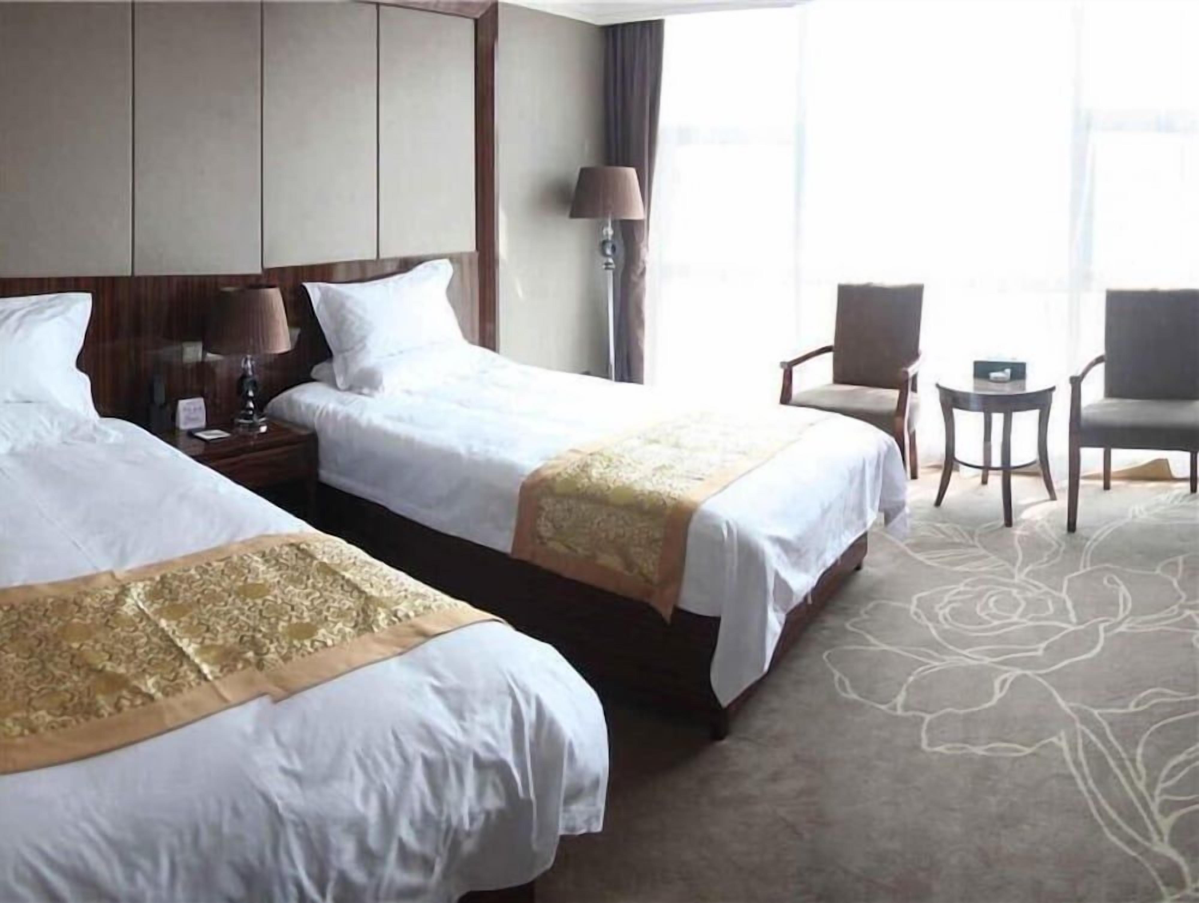 Een hotelkamer met twee bedden, een nachtkastje, een lamp, een stoel en een tafeltje.