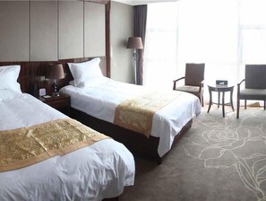 A hotel room with two beds, a nightstand, a lamp, a chair, and a small table.