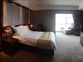 A hotel room with a large bed, bedside lamps, a desk, and a chair.