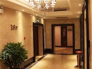Un vestíbulo de hotel con piso de mármol, una planta en maceta, un candelabro y un letrero que indica la habitación 18F.