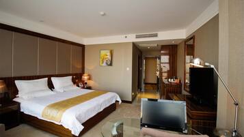 A hotel room with a large bed, a desk with a laptop, a TV, and a glass table.