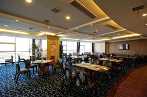 Un comedor de hotel con mesas y sillas, ventanas amplias y una alfombra estampada.