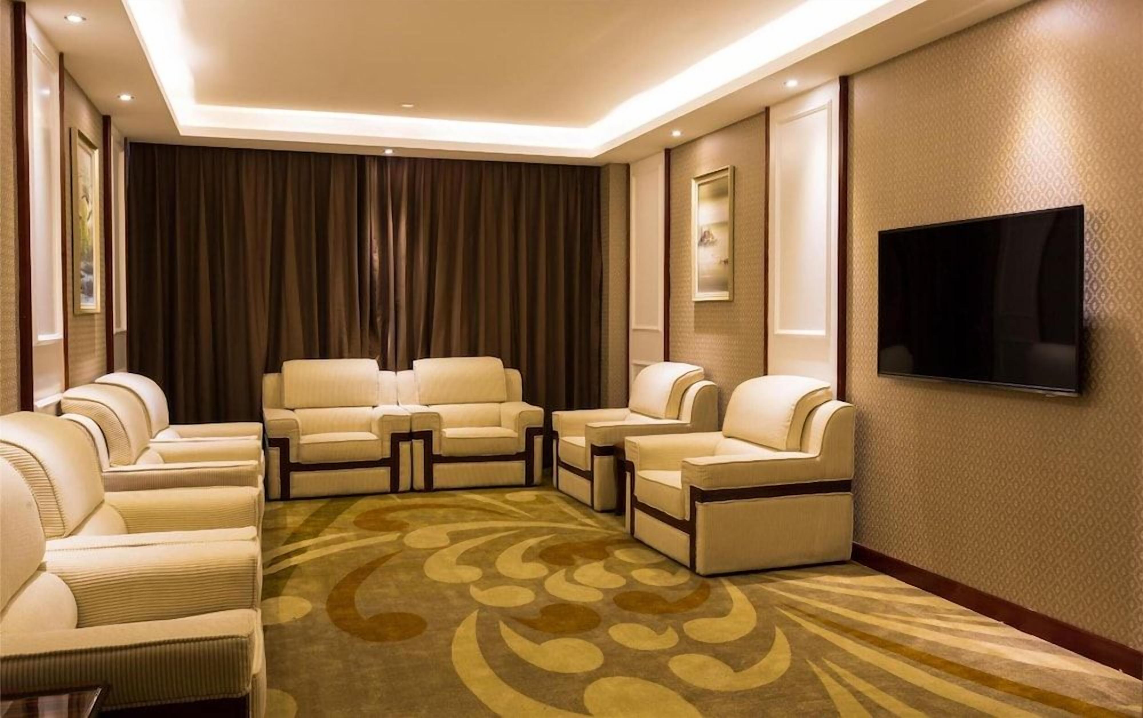 Ett hotellrum med en sittgrupp bestående av soffor och fåtöljer, en platt-TV som är monterad på väggen och en mönstrad matta.
