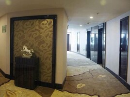 Un pasillo de hotel con alfombra estampada, una estatua sobre un pedestal y una puerta con marco decorativo.