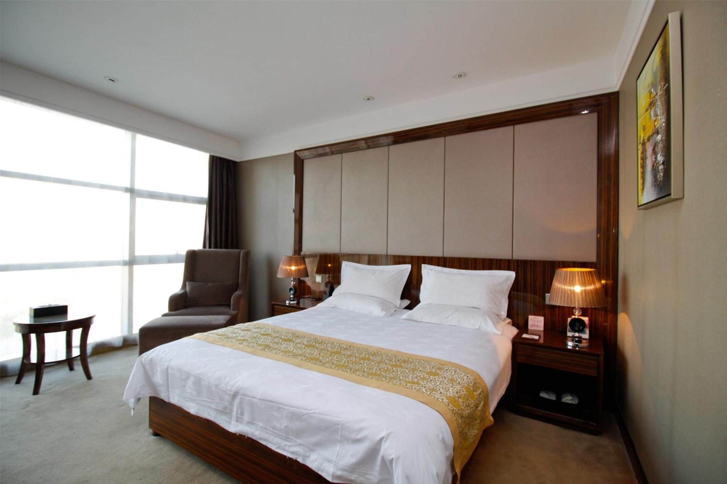 Habitación de hotel con una cama grande, una silla, una mesita y una mesita de noche con lámparas.