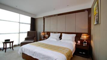 Habitación de hotel con una cama grande, una silla, una mesita y una mesita de noche con lámparas.
