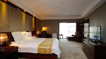 A hotel room with a large bed, a TV, a desk, and a chair.