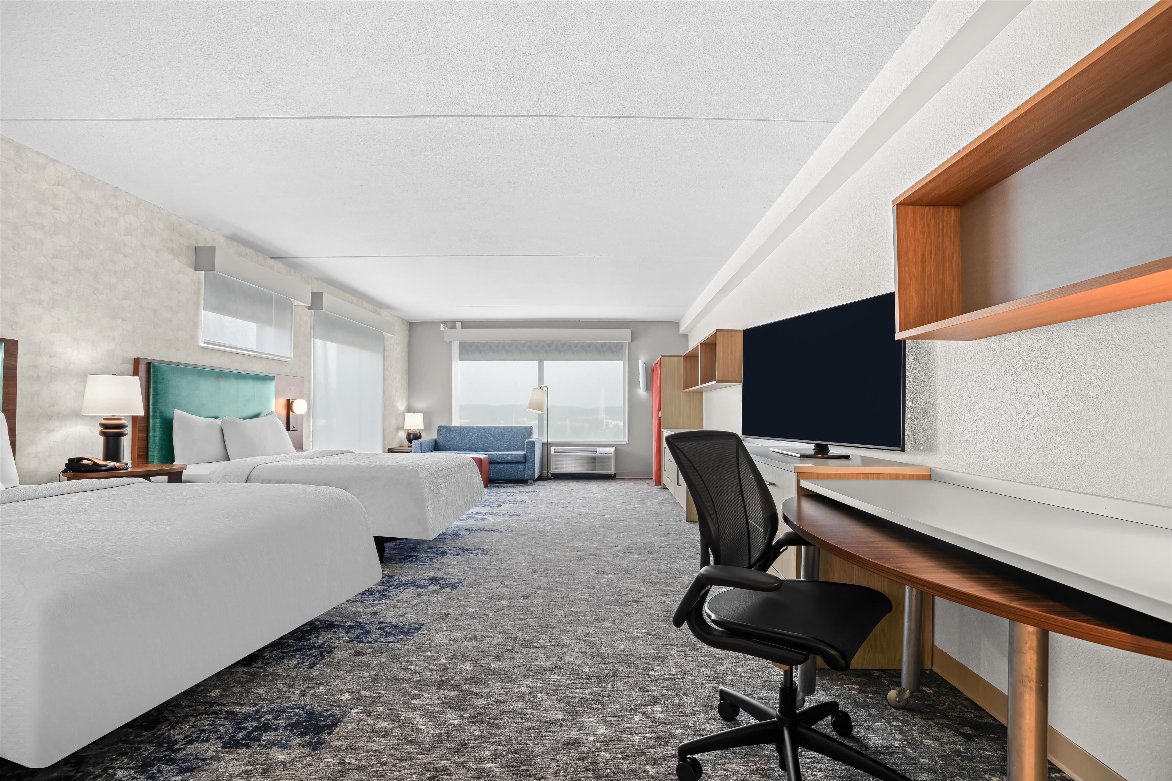 Een hotelkamer met twee bedden, een bureau, een stoel, een televisie en een groot raam.
