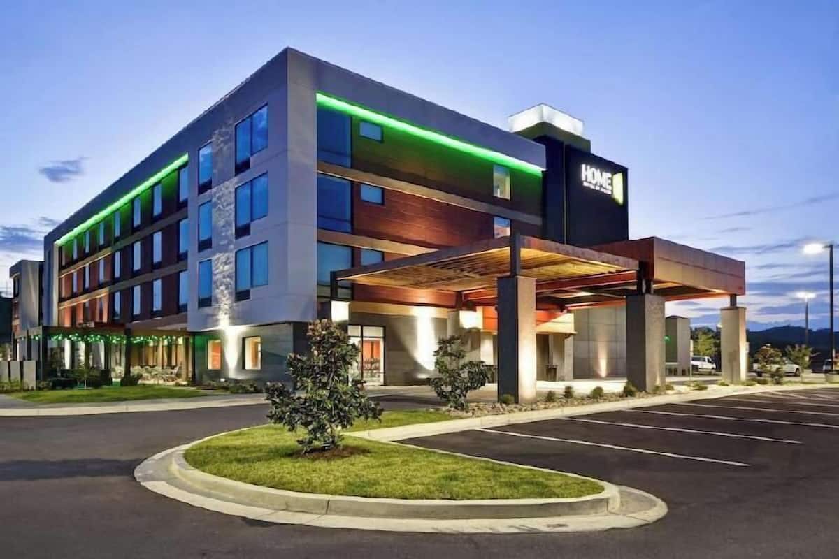 Ein modernes Hotel mit überdachter Einfahrt, mehreren Etagen und einem Parkplatz.