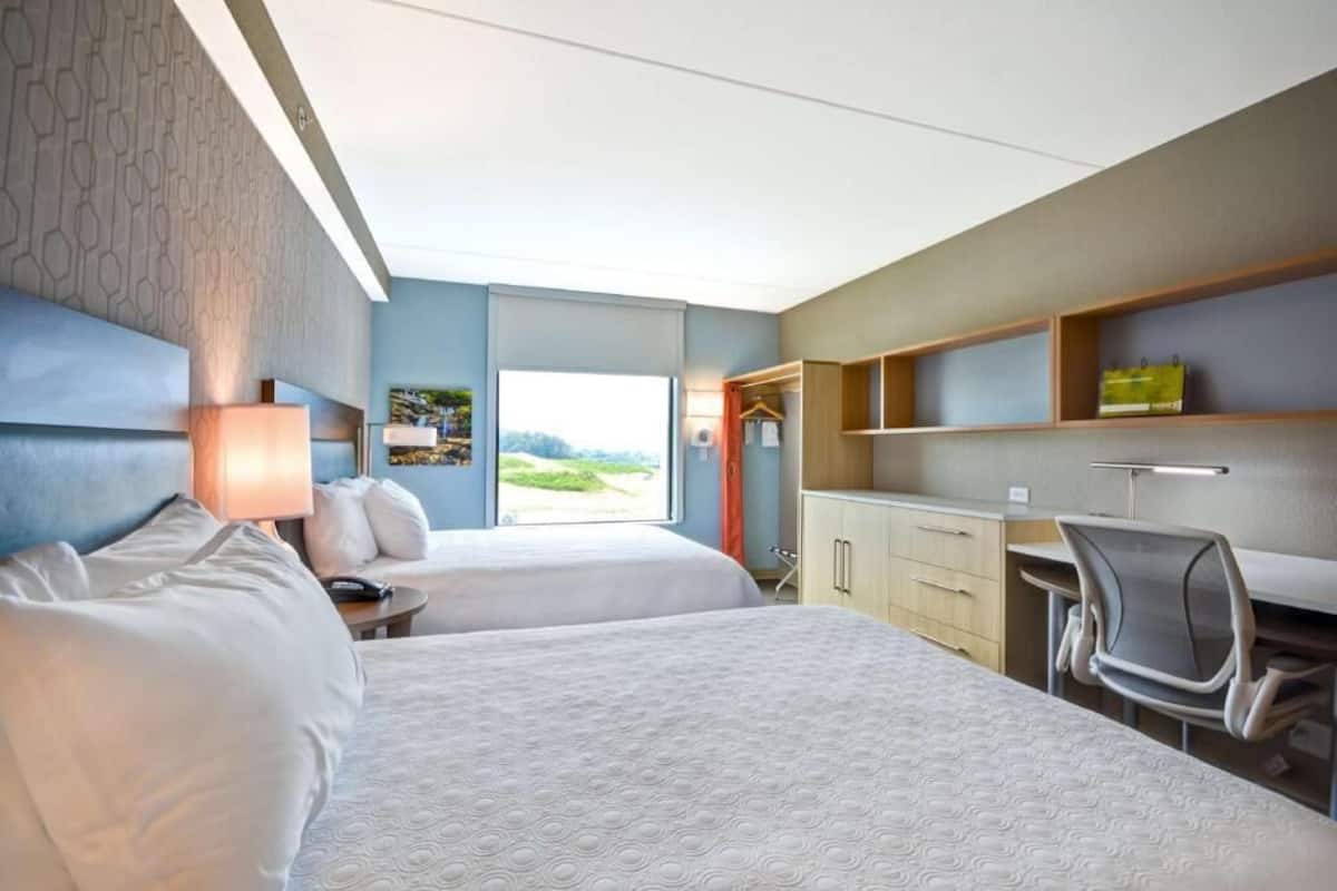 Ein Hotelzimmer mit zwei Betten, einem Schreibtisch, einem Stuhl, einem Kleiderschrank und Blick ins Freie.
