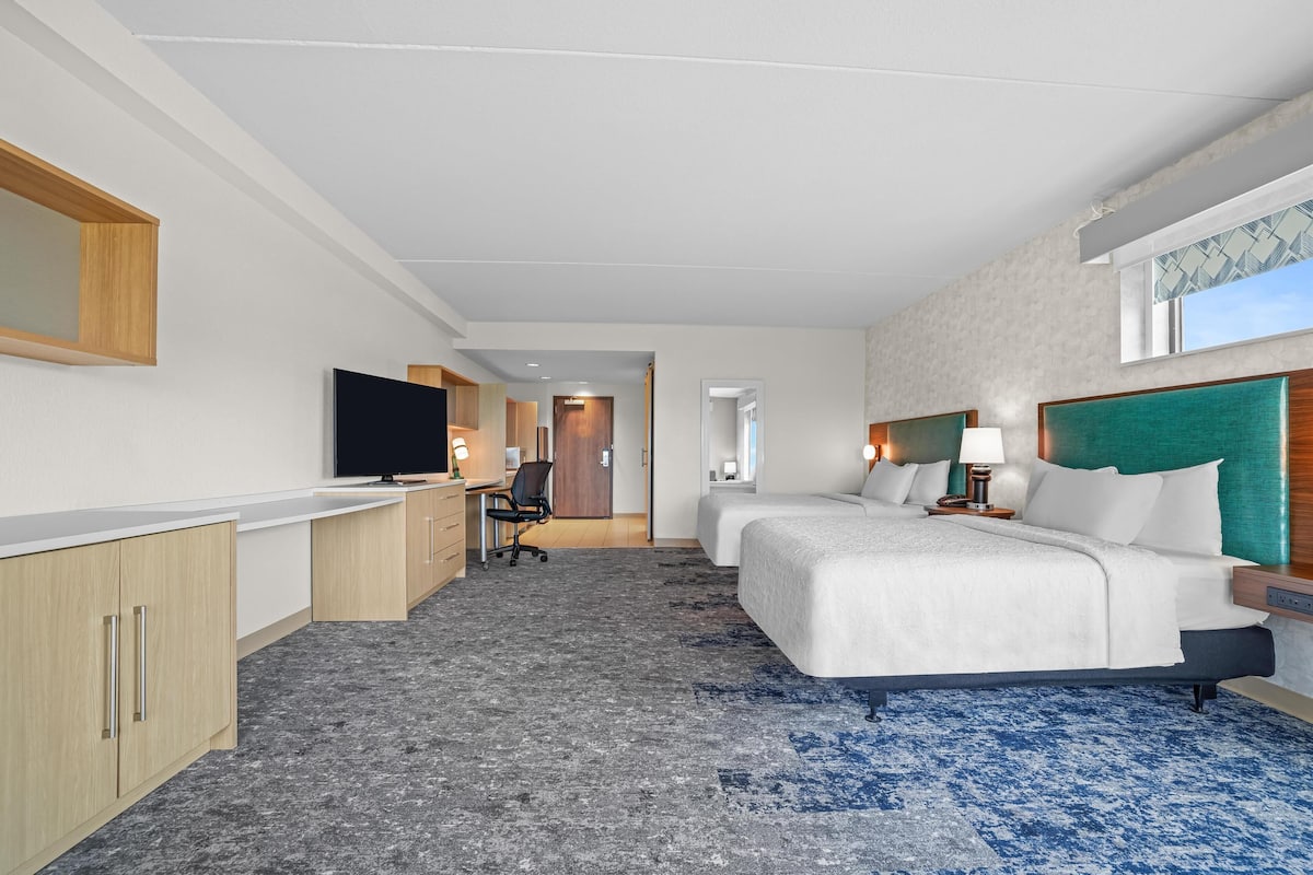 Ein Hotelzimmer mit zwei Betten, einem Schreibtisch, einem Fernseher und einem durchgegangenen Tür erkennbaren Badezimmer.
