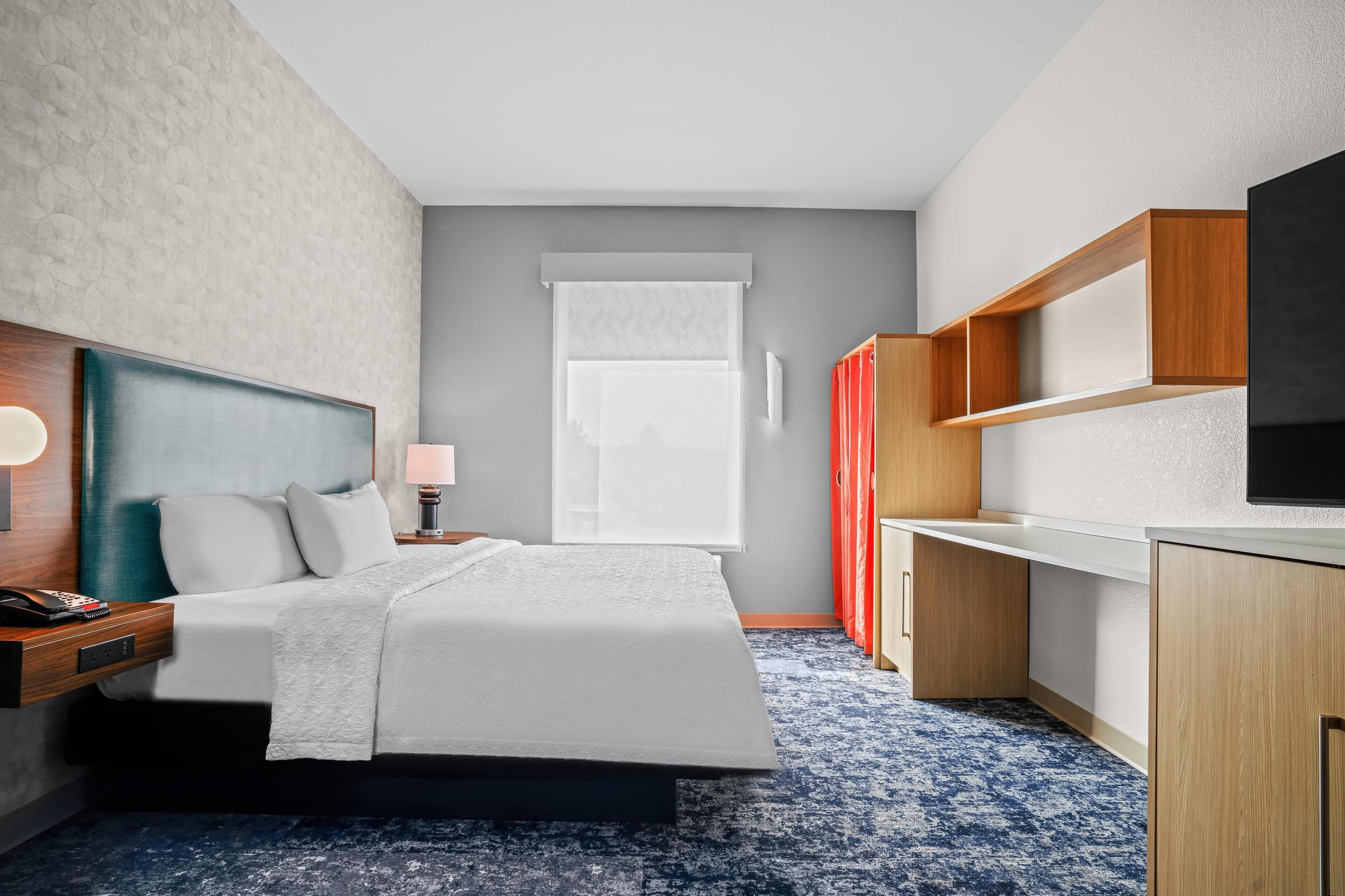 A modern hotel room with a large bed, a desk, and a television.