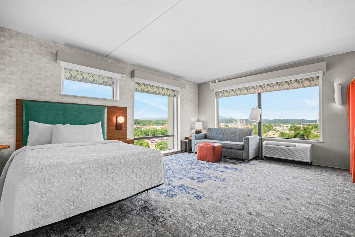Ein Hotelzimmer mit einem großen Bett, einem Sofa, einem Sessel und Blick auf die Stadt.