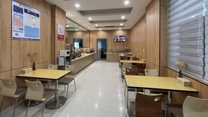 Een moderne eetruimte met houten lambrisering, een balie met horeca-apparatuur, en een televisiescherm.