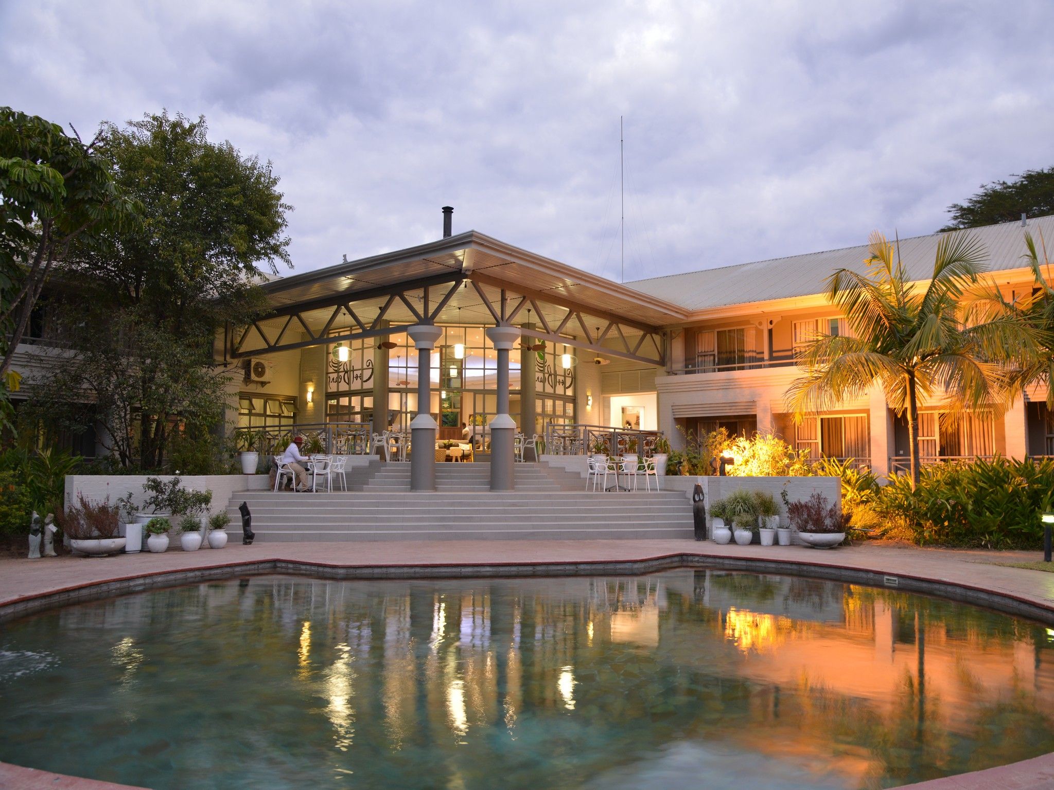Un hotel con piscina, mobiliario exterior y un patio cubierto.