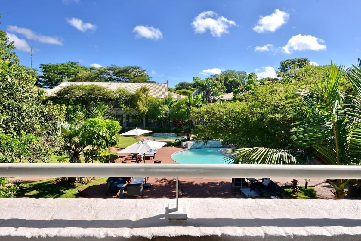 A pool area with lounge chairs and umbrellas, surrounded by lush greenery and trees.