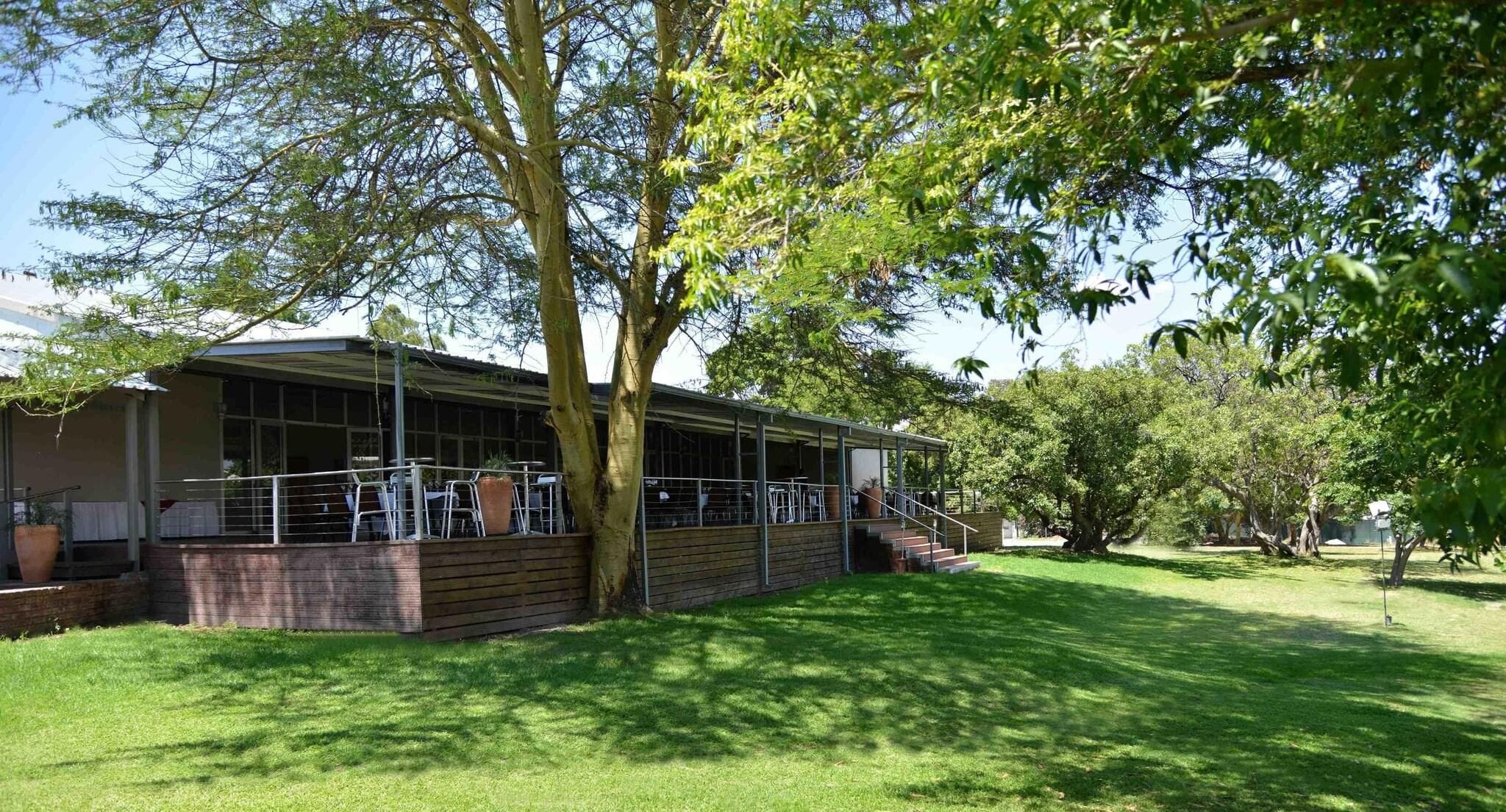 Un edificio con zona de estar al aire libre techada, rodeado de árboles y césped.