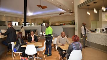 A modern cafe with a high ceiling, ceiling fans, and a seating area with tables and chairs.