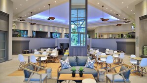 Een ruime lobby met een hoge plafond, diverse zithoeken en een centrale zuil.