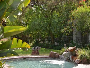 Un jardin avec une piscine, entouré d’une végétation luxuriante et de rochers.