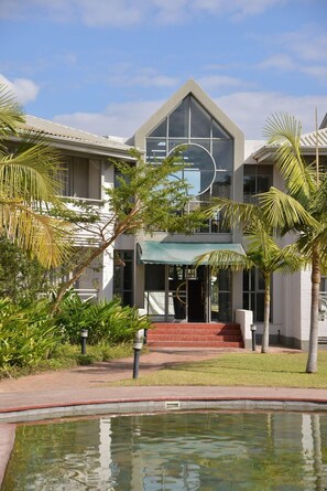 A modern building with a large glass facade, a pool, and tropical landscaping. - Cresta Lodge Harare (Harare)