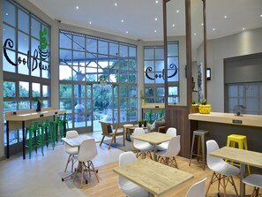 Un interior de cafetería moderno con amplios ventanales, sillas verdes y blancas y mesas de madera.
