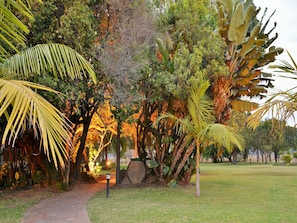 A pathway leading through a lush garden with various tropical plants and a stone structure. - Cresta Lodge Harare (Harare)