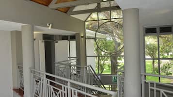 A multi-level interior with a staircase, white railings, and large windows offering a view of greenery outside.