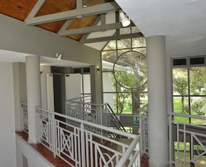 A multi-level interior with a staircase, white railings, and large windows offering a view of greenery outside. - Cresta Lodge Harare (Harare)