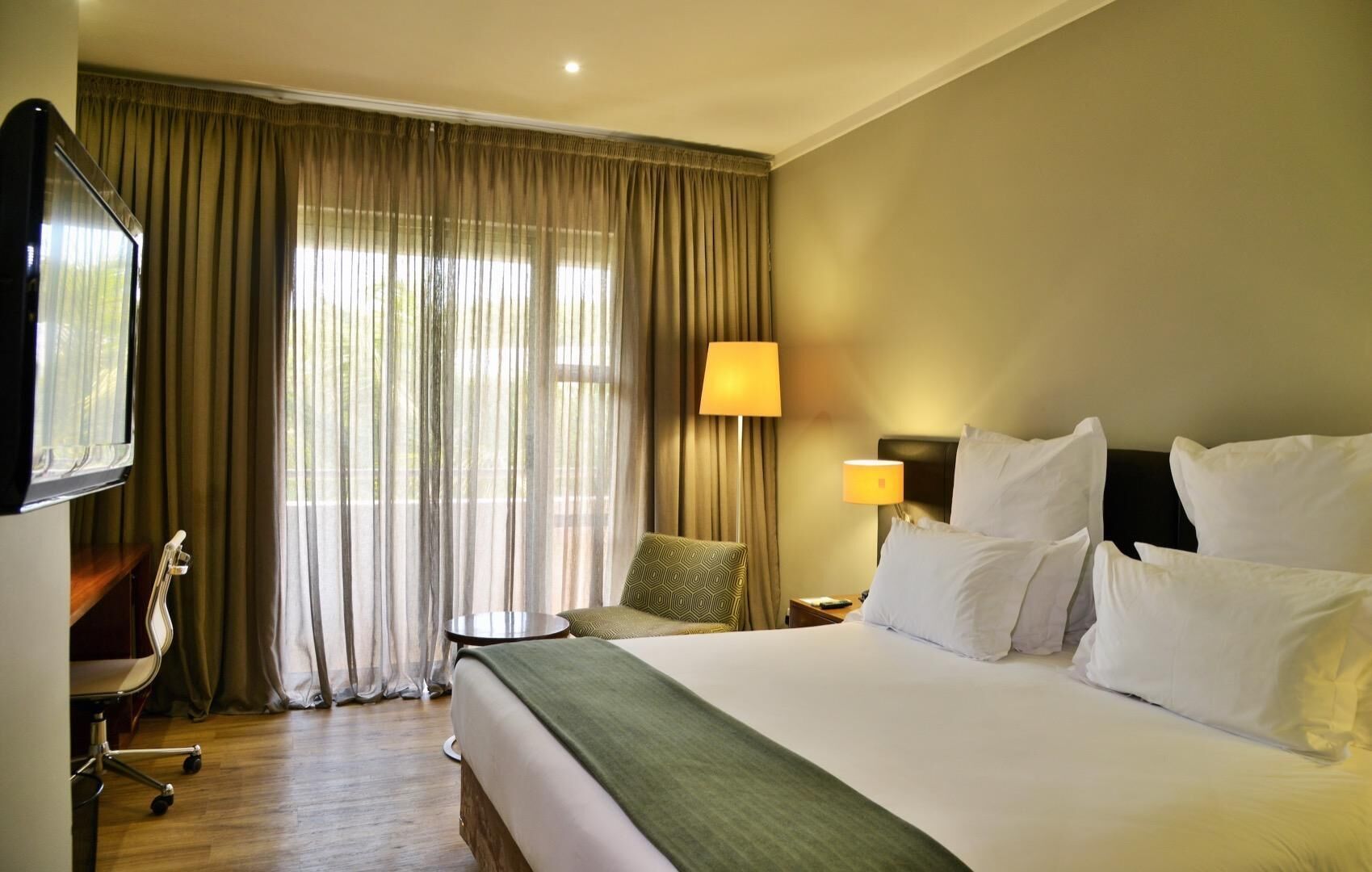 A hotel room with a bed, two bedside lamps, a TV, a chair, and a desk.