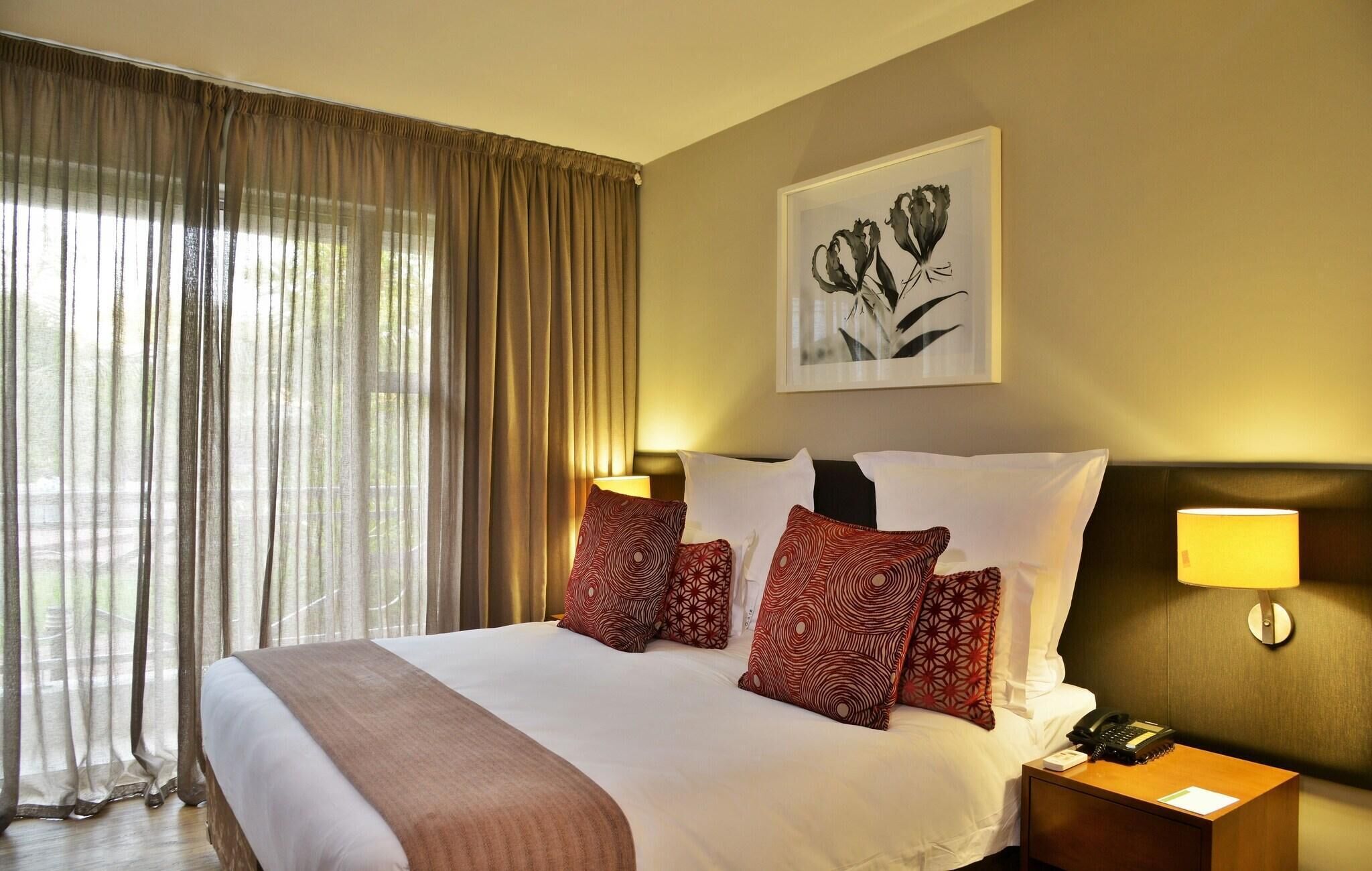 A hotel room with a large bed, a bedside table with a lamp, and a framed floral artwork on the wall.