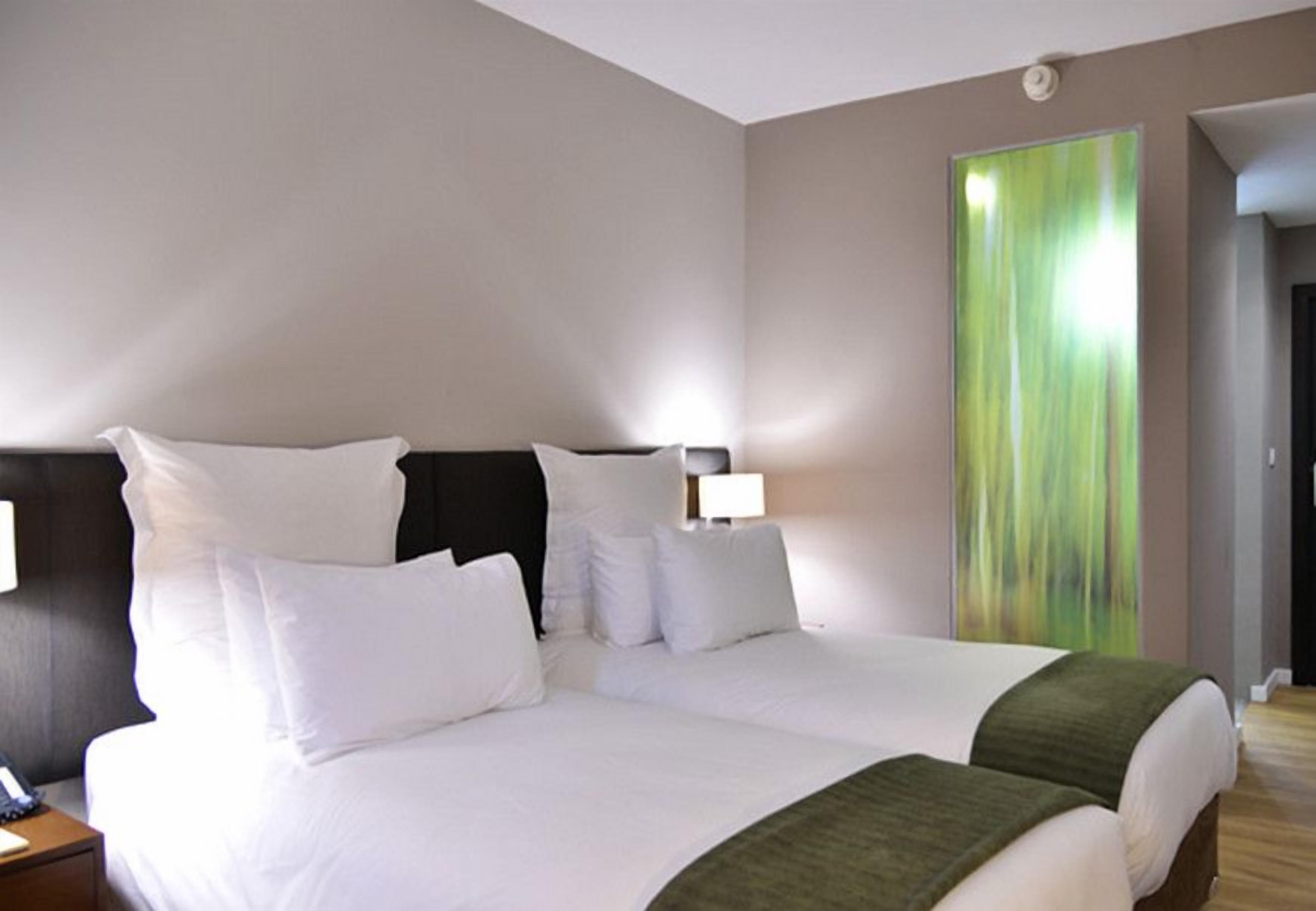 A hotel room with a large bed, two bedside tables, and a green abstract painting on the wall.