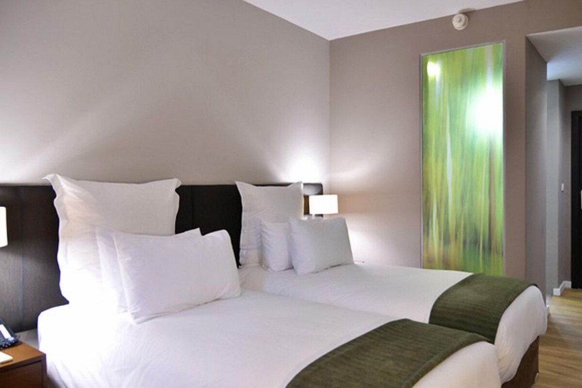 A hotel room with a large bed, two bedside tables, and a green abstract painting on the wall.