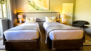 Een hotelkamer met twee bedden, een hoofdeinde, bedlampjes, een stoel en een schilderij aan de muur.