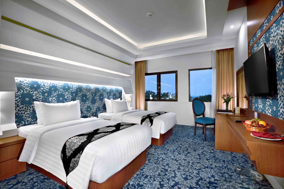 Une chambre d’hôtel avec deux lits, un bureau avec une chaise, une télévision et une fenêtre donnant sur un paysage agréable.