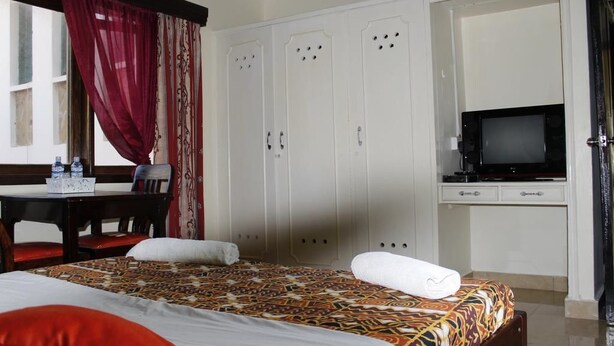 Ein Hotelzimmer mit einem Bett, einem Schreibtisch mit Stuhl, einem Fernseher und einem Kleiderschrank.