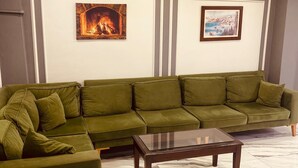Een woonkamer met een groene bank, een glazen salontafel en twee ingelijste foto’s aan de muur.
