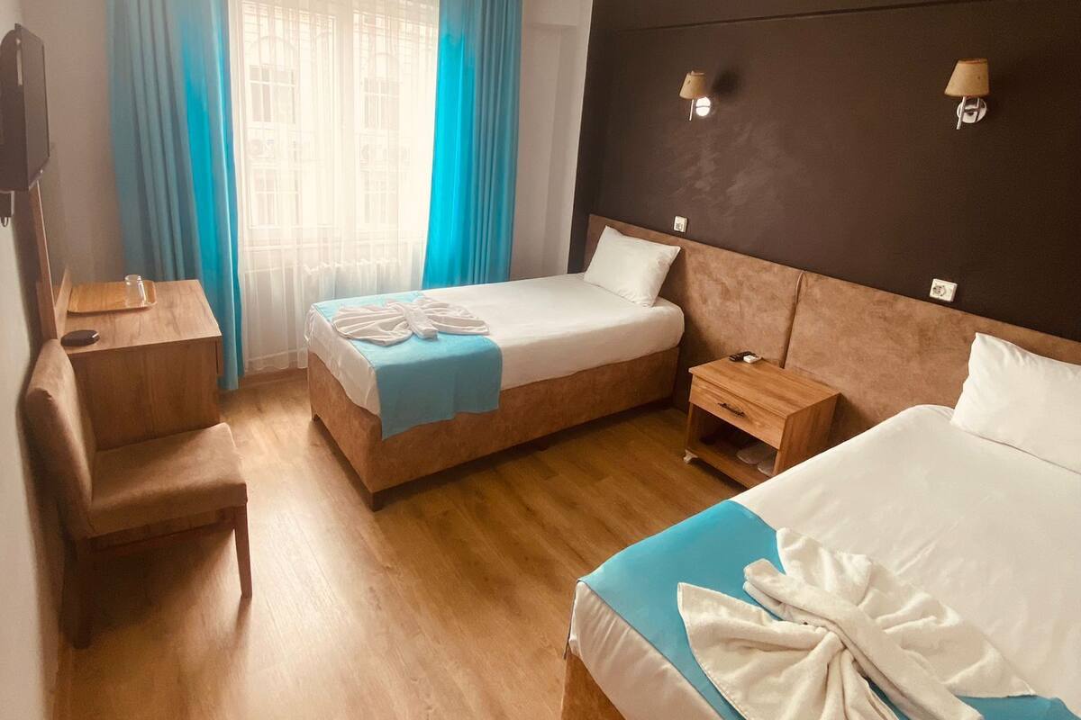 Une chambre d’hôtel avec un lit, un bureau, une chaise, une table de chevet et une fenêtre avec des rideaux.