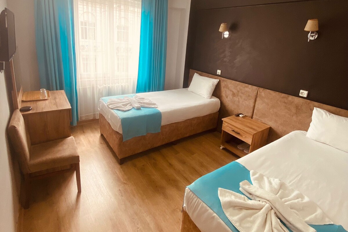 A hotel room with a bed, a desk, a chair, a nightstand, and a window with curtains.