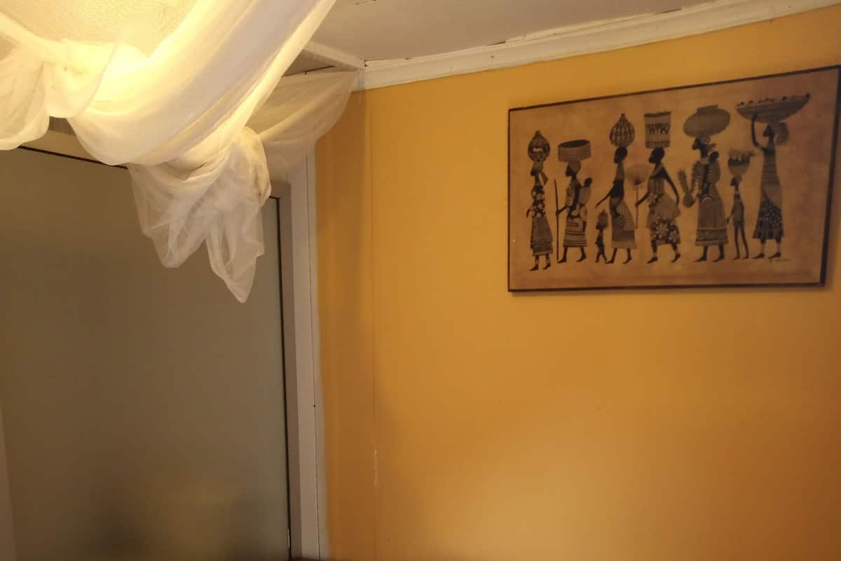Ein Schlafzimmer mit einem Bett, einem Nachttisch, einem Wandbild und einem transparenten Baldachin.