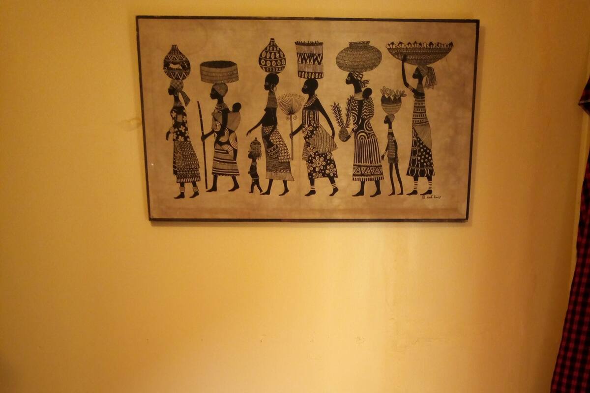 Ein Bett mit weißer Bettwäsche und einem gerahmten Kunstwerk, das Figuren mit Körben auf dem Kopf zeigt.