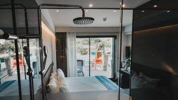 A modern hotel room with a large bed, a glass shower enclosure, and a balcony with outdoor seating.