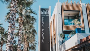 Un edificio con un letrero que dice "H-BOUTIQUE PENA PARDA" y un diseño arquitectónico moderno con listones de madera y ventanas de vidrio.
