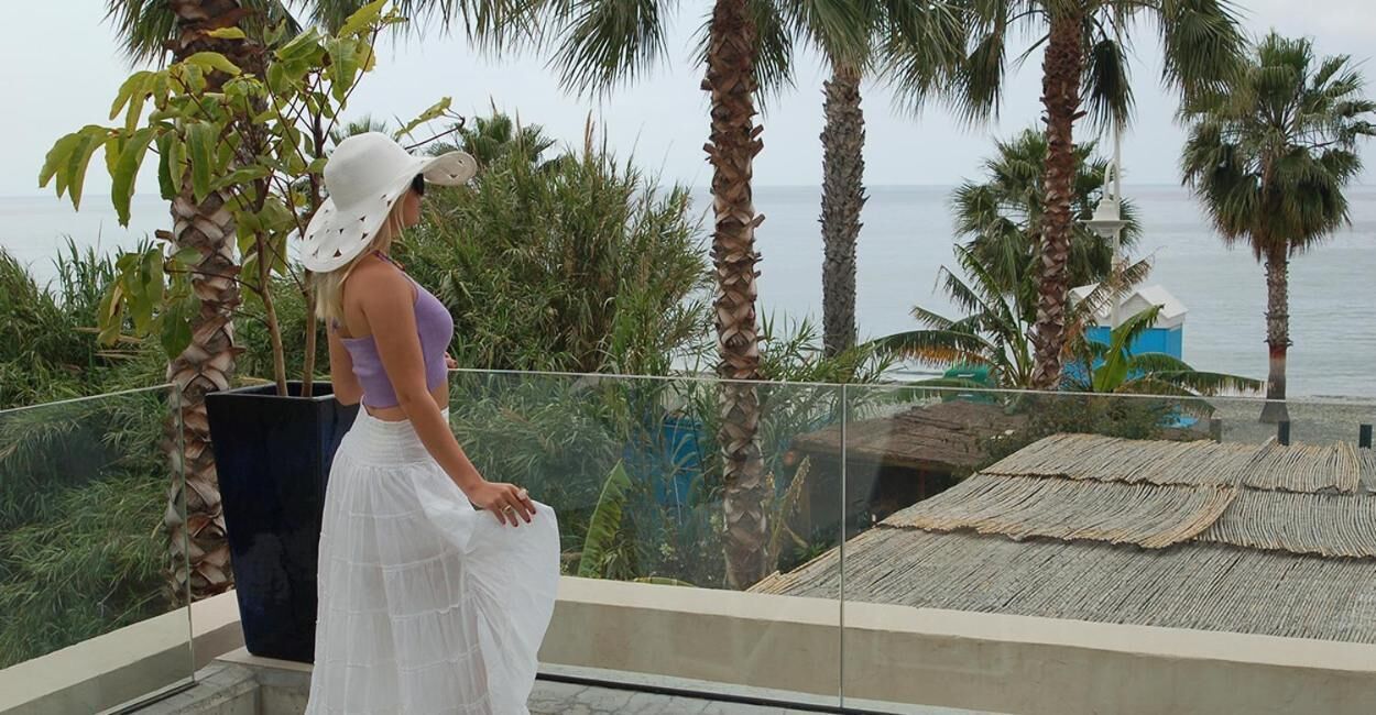 A balcony with a view of the sea, surrounded by palm trees and a tropical garden.