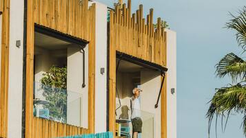 Un edificio moderno con due ingressi aperti, un recinto in legno e una persona in piedi sul balcone.