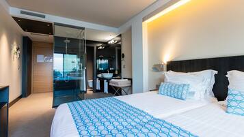 A modern hotel room with a large bed, a bathroom with a sink and mirror, and a view through a glass door.