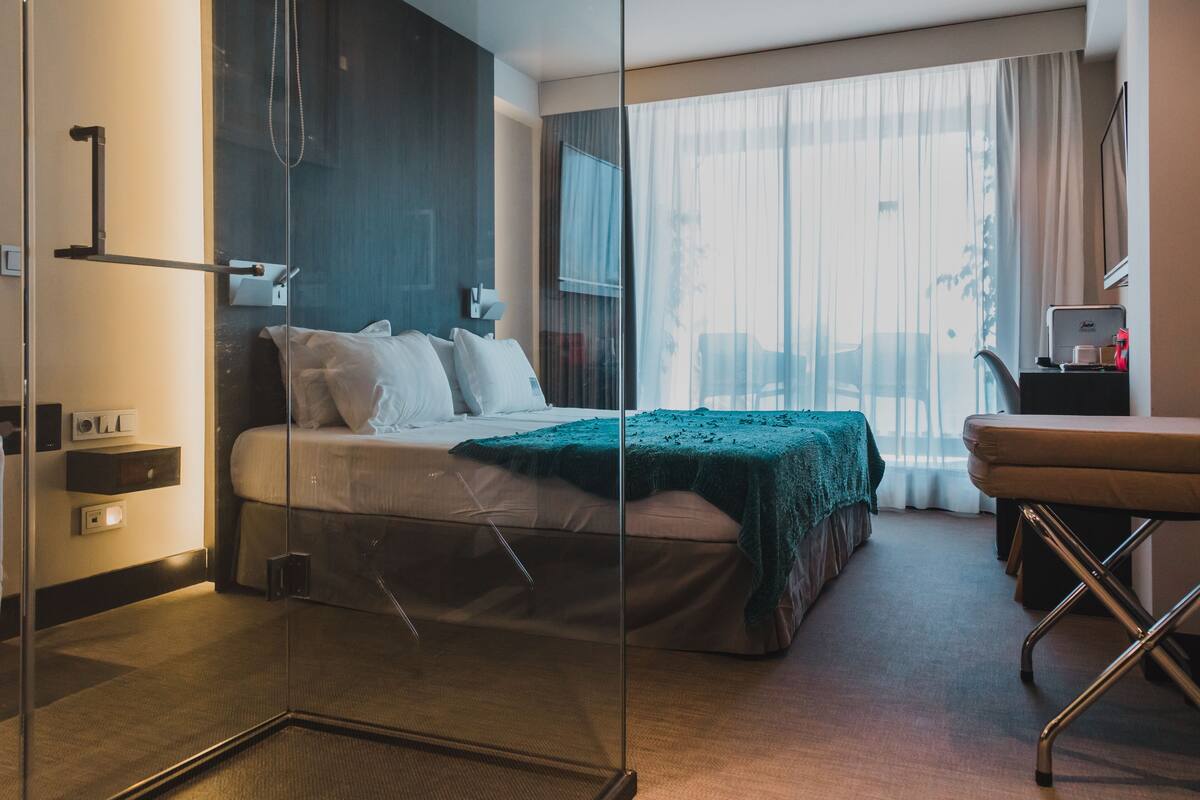 A modern hotel room with a glass partition separating the bed area from the sitting area.