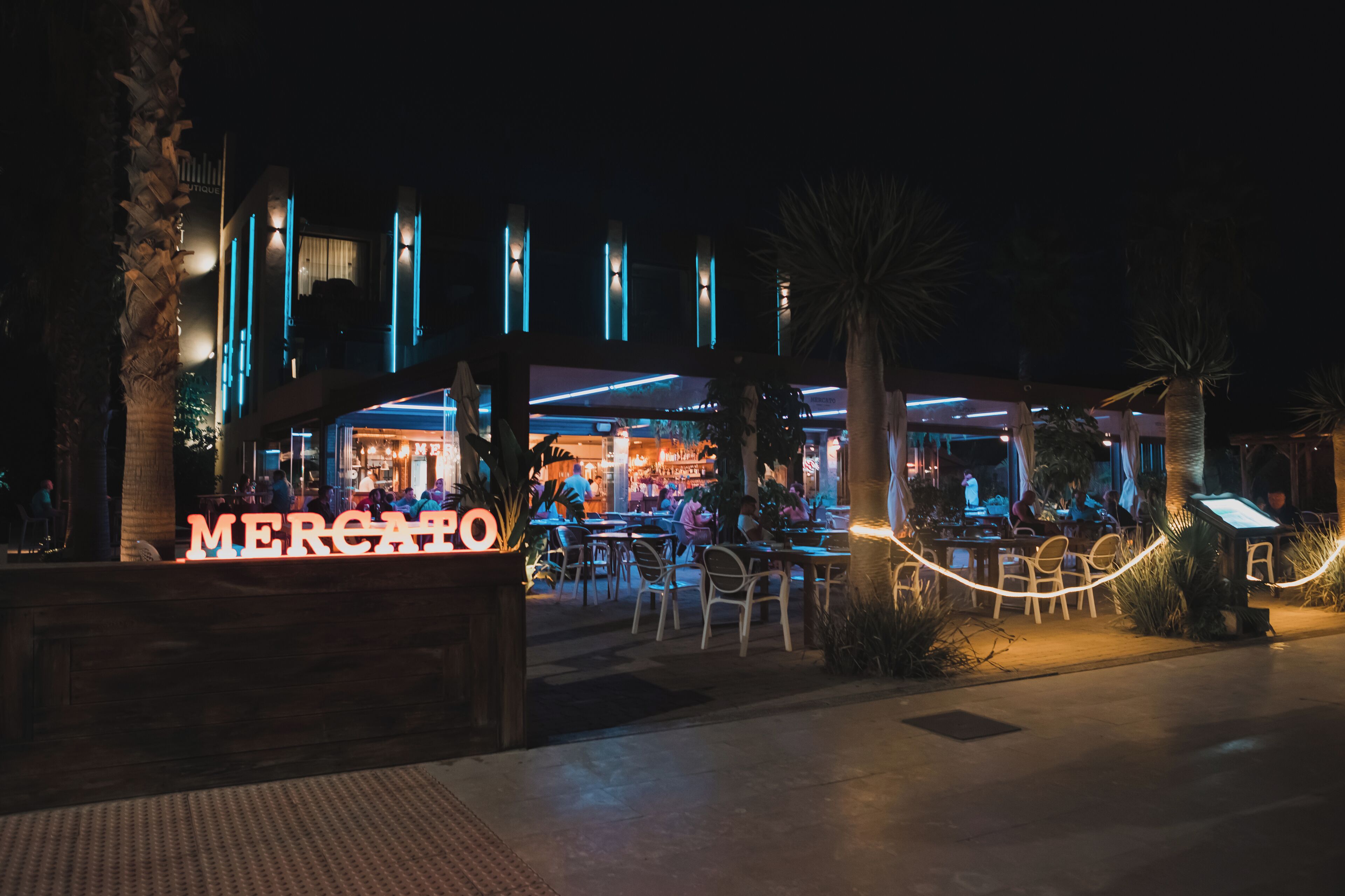 Un área de comedor al aire libre con un letrero que dice "MERCATO" y mesas y sillas dispuestas para los clientes.