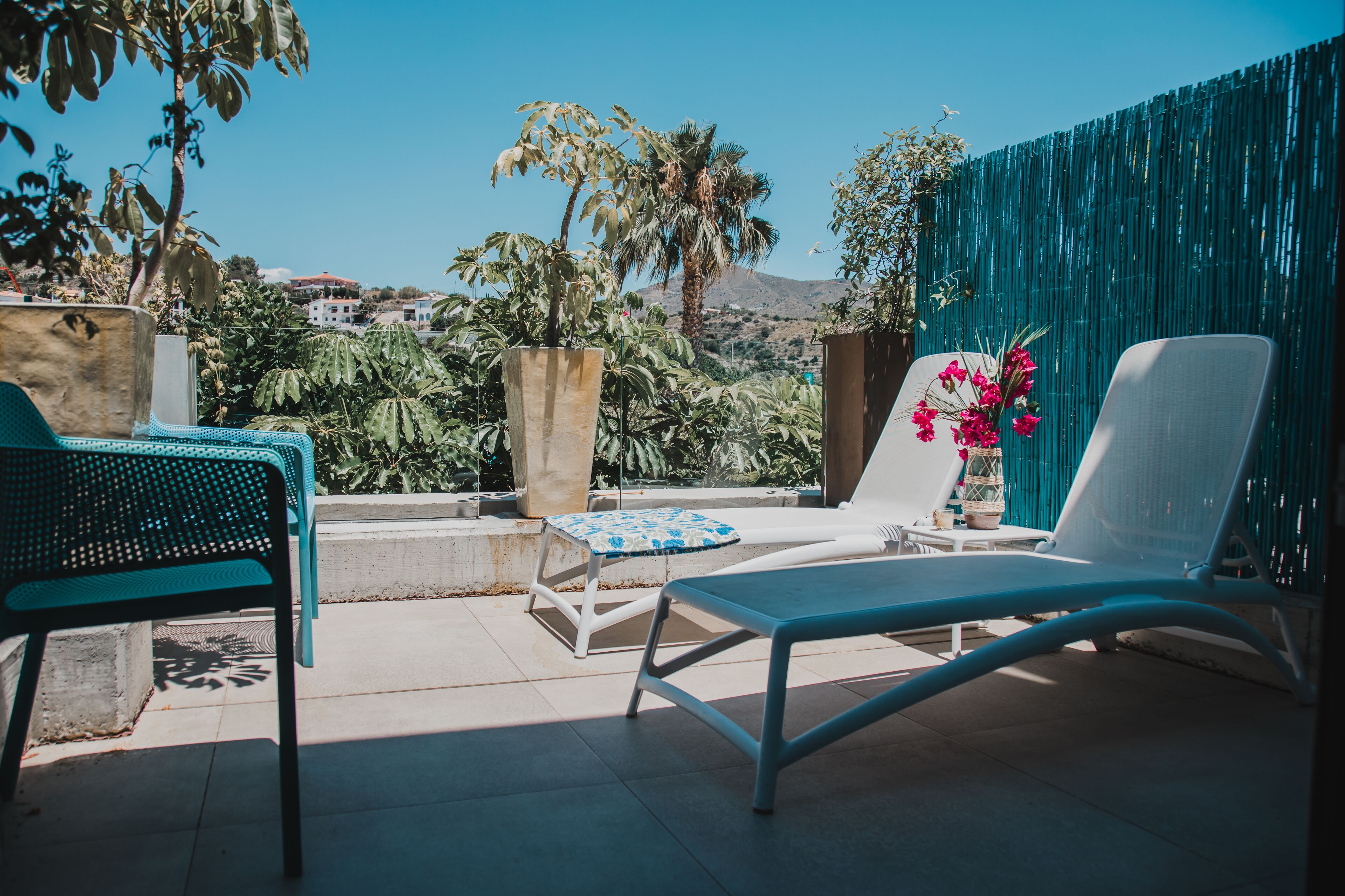 Eine Terrasse mit einer weißen Liege, einem blauen Sessel und einem kleinen Tisch mit einer blau-weißen Tischdecke.